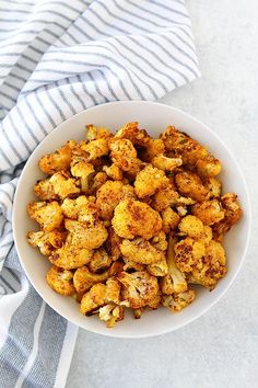 a white bowl filled with roasted cauliflower on top of a blue and white towel