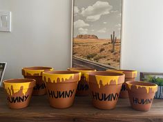 six planters with painted words on them sitting on a table in front of a painting