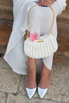 a woman in white dress and heels holding a handbag with flowers on it's side