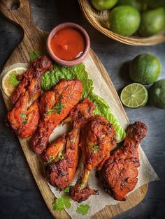 chicken wings with lettuce and sauce on a cutting board next to limes