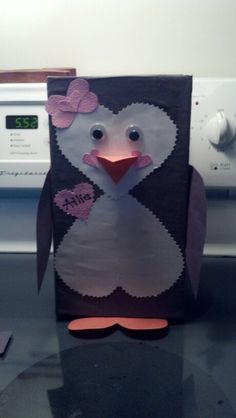 a penguin made out of paper on top of a microwave oven with a pink bow around its neck