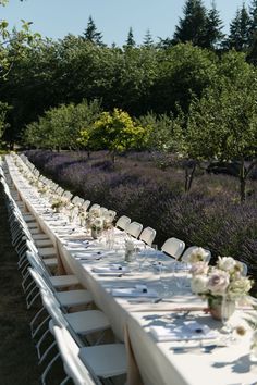 a long table is set with white linens and place settings for an outdoor dinner