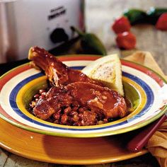 a plate topped with meat and beans next to an open crockpot on a table