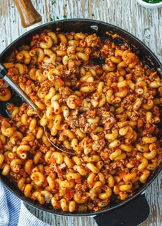 a skillet filled with macaroni and cheese on top of a wooden table