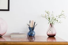 two vases with flowers and books on a table next to a wall mounted mirror