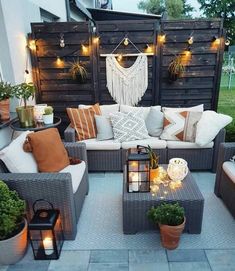 an outdoor seating area is decorated with lights and pillows, potted plants on either side of the couch