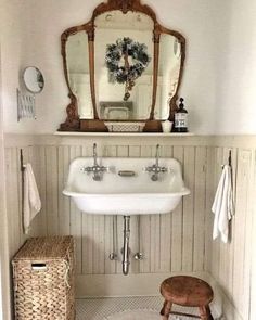 a white sink sitting under a bathroom mirror next to a wooden stool with a basket underneath it