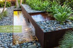 an outdoor garden with rocks and water flowing from the trough to the ground, surrounded by greenery