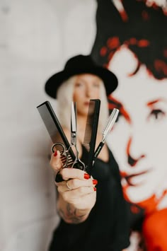 a woman holding scissors in front of a wall with a painting on it's side