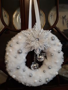 a white wreath with silver ornaments hanging from it's front door, on top of a table