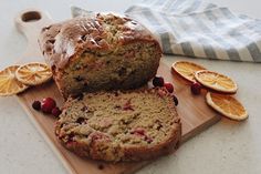 a loaf of fruity bread on a cutting board with sliced oranges and cranberries