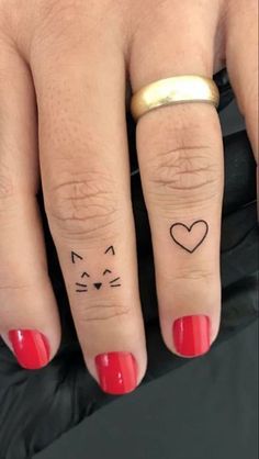 two fingers with tattoos on them, one has a cat and the other has a heart