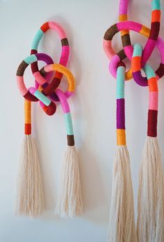 two wall hangings made out of yarn and tassels on the side of a white wall