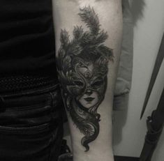 a woman's arm with a mask and feathers tattoo on her left arm,