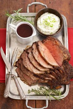 a tray with meat, mashed potatoes and sauces on it next to utensils