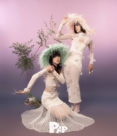 two women dressed in white and green are posing for the camera with one woman wearing a feathered hat