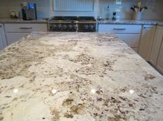 a kitchen counter top with white cabinets and an oven in the backgrounnd