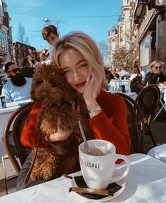 a woman sitting at a table with a coffee cup and teddy bear in her lap