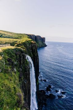 a large waterfall flowing into the ocean next to a lush green hillside covered in grass