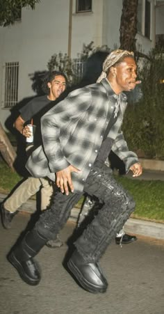 a man walking down the street with his foot in the air while wearing black boots