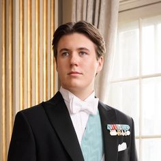 a man in a tuxedo and bow tie standing next to a window with curtains