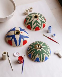 three painted pots sitting on top of a table next to paintbrushes and paints