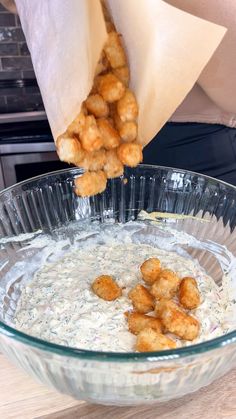 a person dipping some tater tots in a glass bowl on top of a wooden table