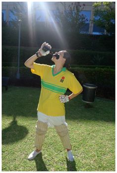 a man dressed as a cricket player drinking from a bottle while standing in the grass