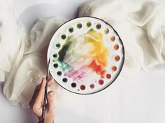 a person is holding a paint palette and painting with watercolors on the plate