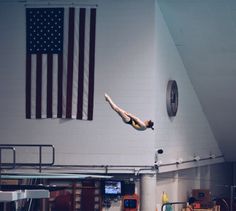 a woman diving into the pool in front of an american flag hanging on the wall