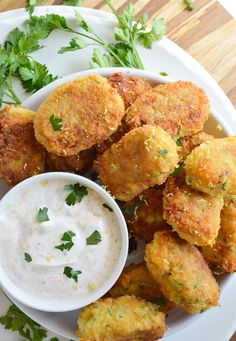 some fried food on a white plate with ranch dip and parsley sprigs