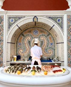 a chef preparing food on top of a white table in front of a mosaic wall