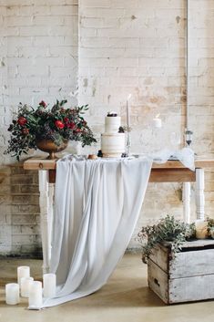 the table is covered with white cloth and decorated with red flowers, candles and greenery