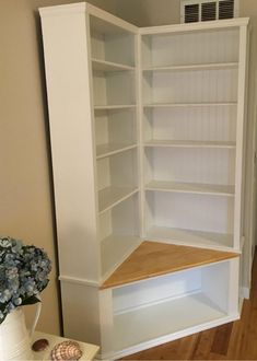 an empty white bookcase in a living room next to a vase with blue flowers