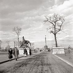 black and white photograph of people walking on dirt road with horse statue in the background