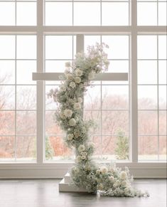 a cross made out of flowers sitting on top of a table next to a window