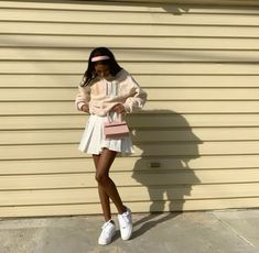 a woman standing in front of a building wearing white sneakers and a pink sweater dress