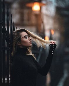 a woman with blonde hair and glasses standing in front of an iron fence on a rainy day