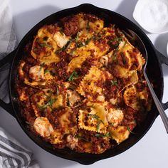 a skillet filled with pasta and sauce on top of a white table next to spoons