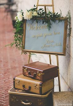 suitcases stacked on top of each other in front of a welcome sign with flowers