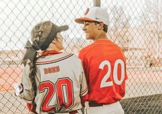 two baseball players standing next to each other in front of a fence and looking at each other