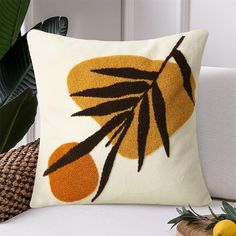 an orange and brown pillow on a white couch next to a potted plant in a wicker basket