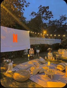 an outdoor movie is set up in the evening with white furniture and lights around it