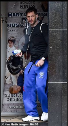 a man in blue sweatpants holding a helmet and listening to music on his headphones