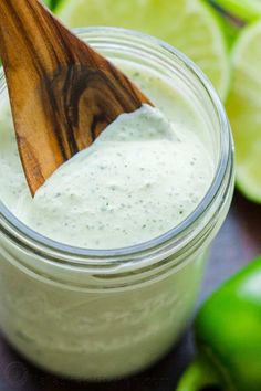 a wooden spoon sticking out of a jar filled with white sauce next to sliced limes