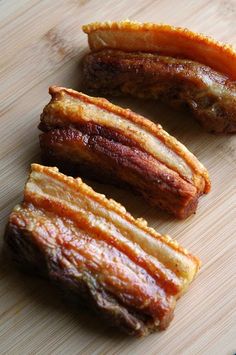 three pieces of bacon sitting on top of a wooden cutting board