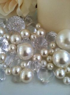 pearls and crystal stones are arranged on a table next to a white candle with a rose in the background