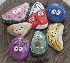 five painted rocks with faces on them sitting on a wooden table next to each other