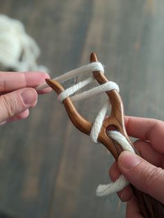 two hands are holding an object made out of wood and white yarn on a wooden table