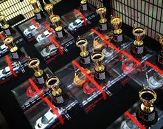 there are many trophies on display in the case with red ribbons around them and cars behind them